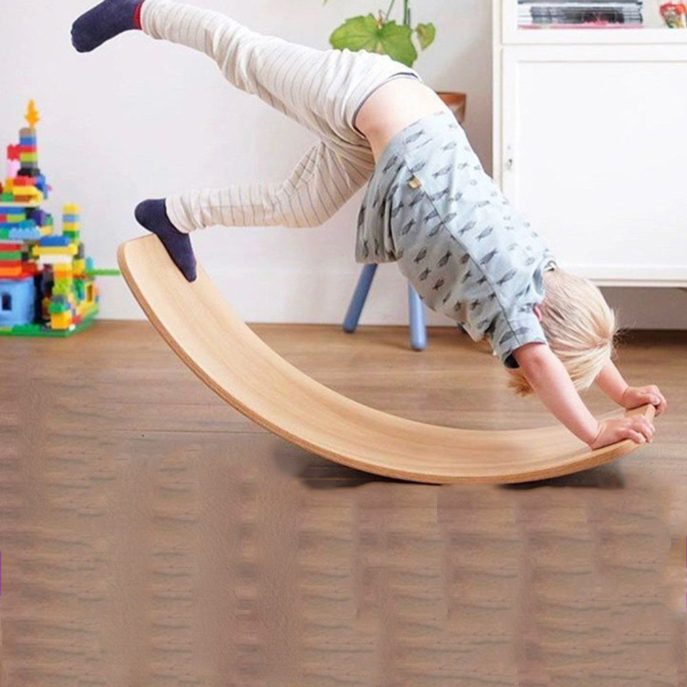 A boy doing a handstand on a natural wooden wobble board indoors