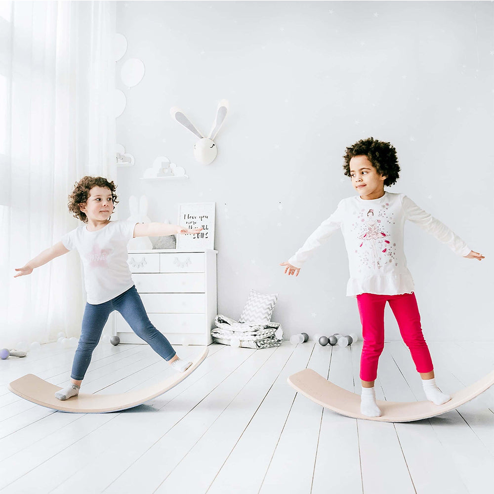 A girl smiling and playing with a natural wooden balance board surrounded by soft balls