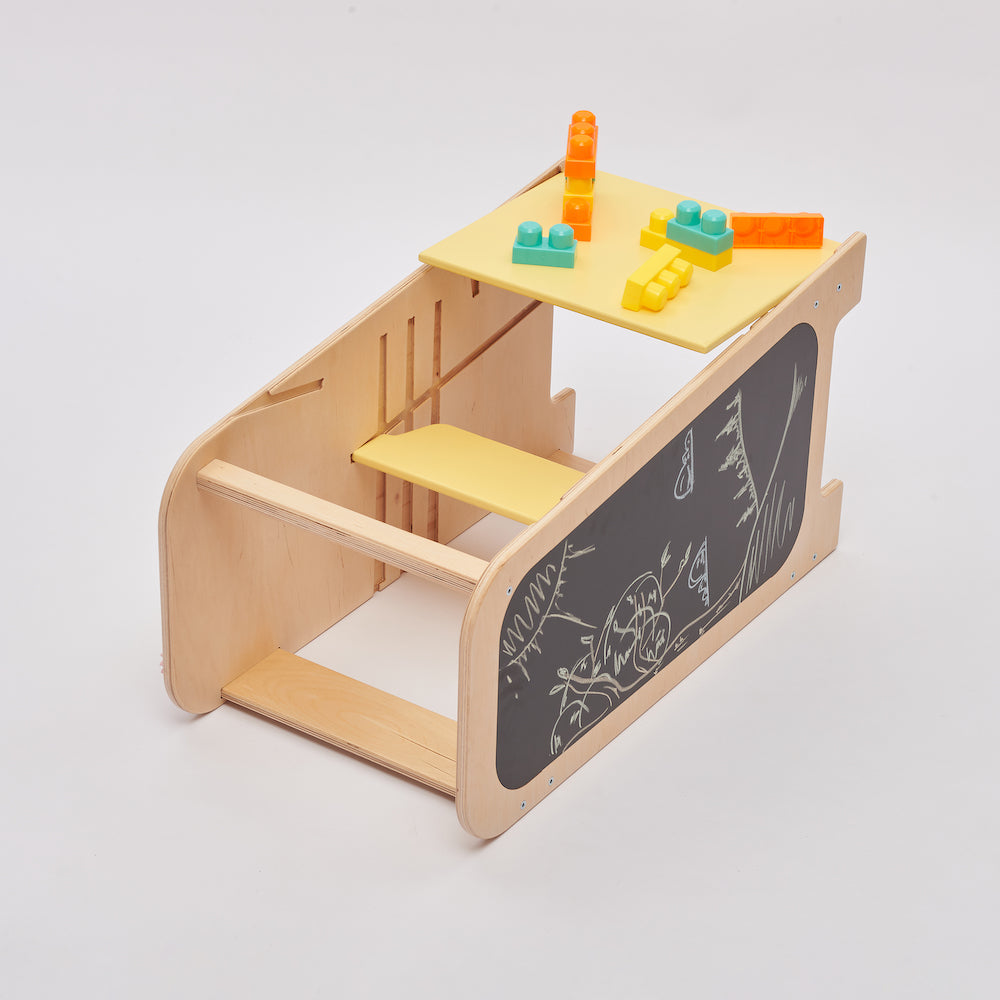 Montessori learning tower made of natural wood with a yellow side busy board, featuring interactive gears, sliders, and lockable elements for toddlers.